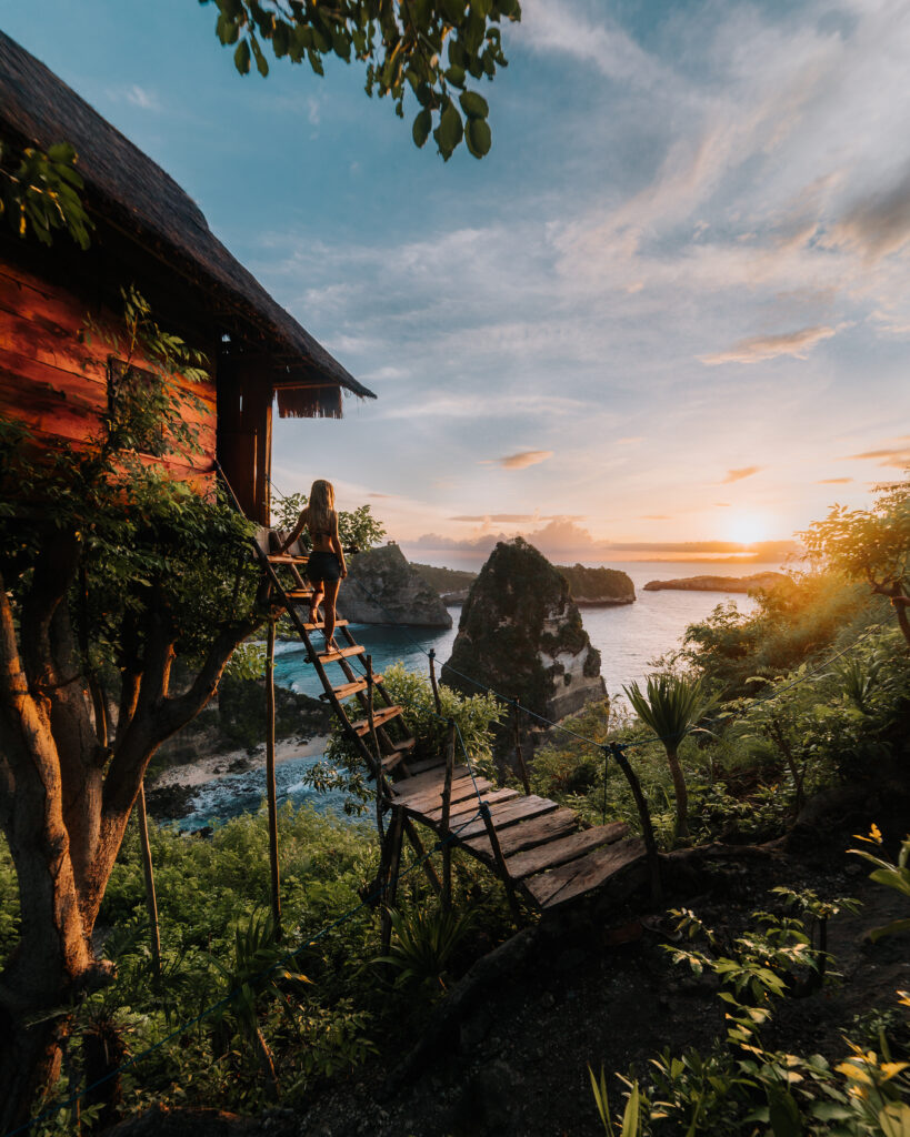 Bree stands on the steps of a treehouse overlooking the ocean at sunset in Bali, Indonesia