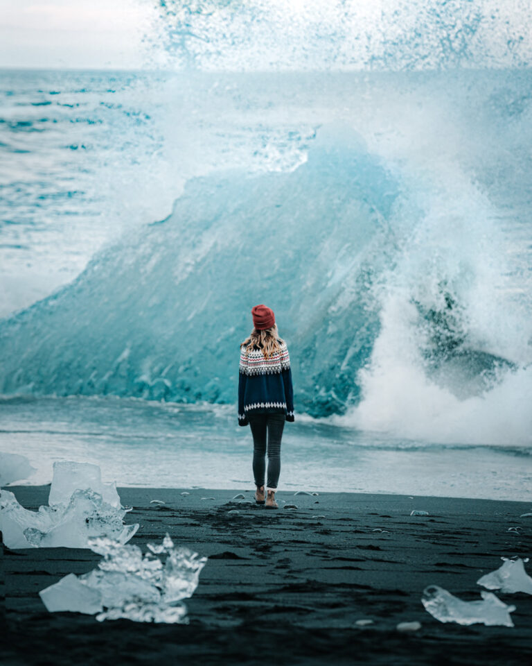 Bree stands on a black sand beach in Iceland looking out at the ocean and a block of ice from a glacier