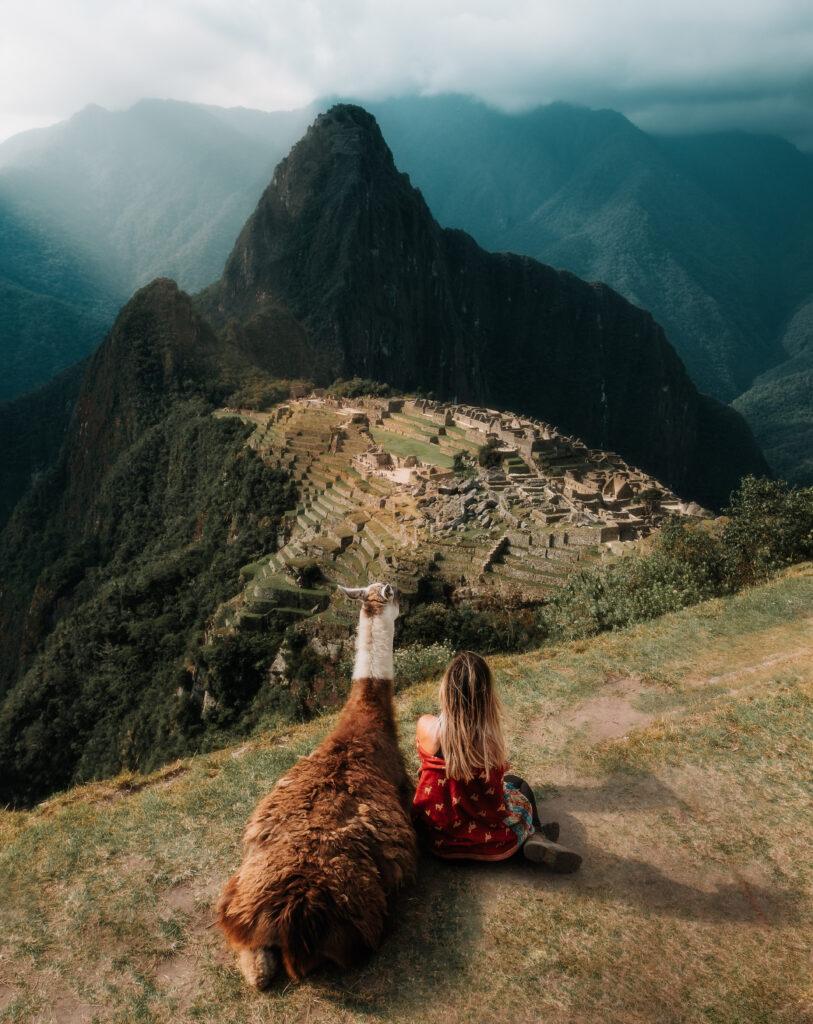 Bree sits next to an alpaca, looking out over Macchu Pichu