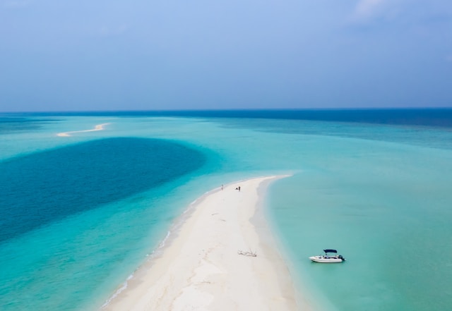 a sliver of white sand in the bright blue ocean in the Maldives on a clear blue day
