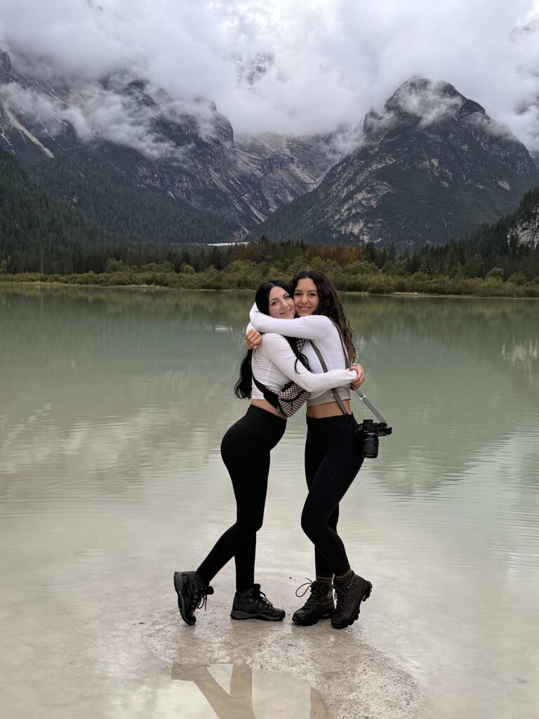 Bree and her friend hug in front of a lake in the Dolomites, Italy