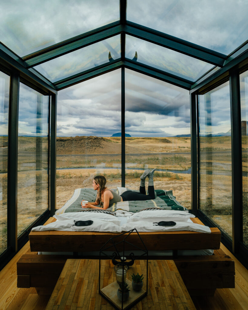 Bree laying on a bed in an all-glass hut